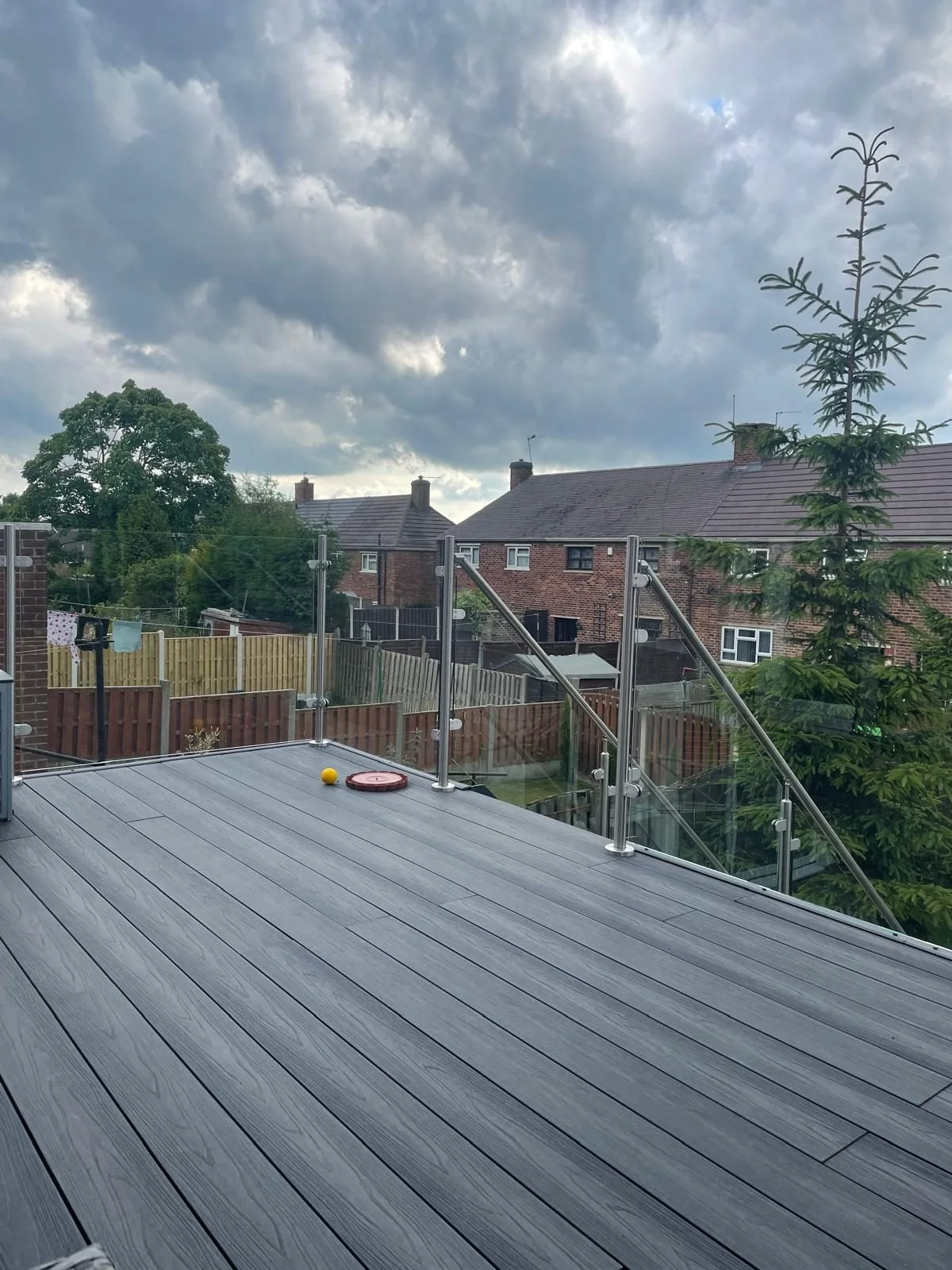 Grey composite decking with a glass balustrade above a garden