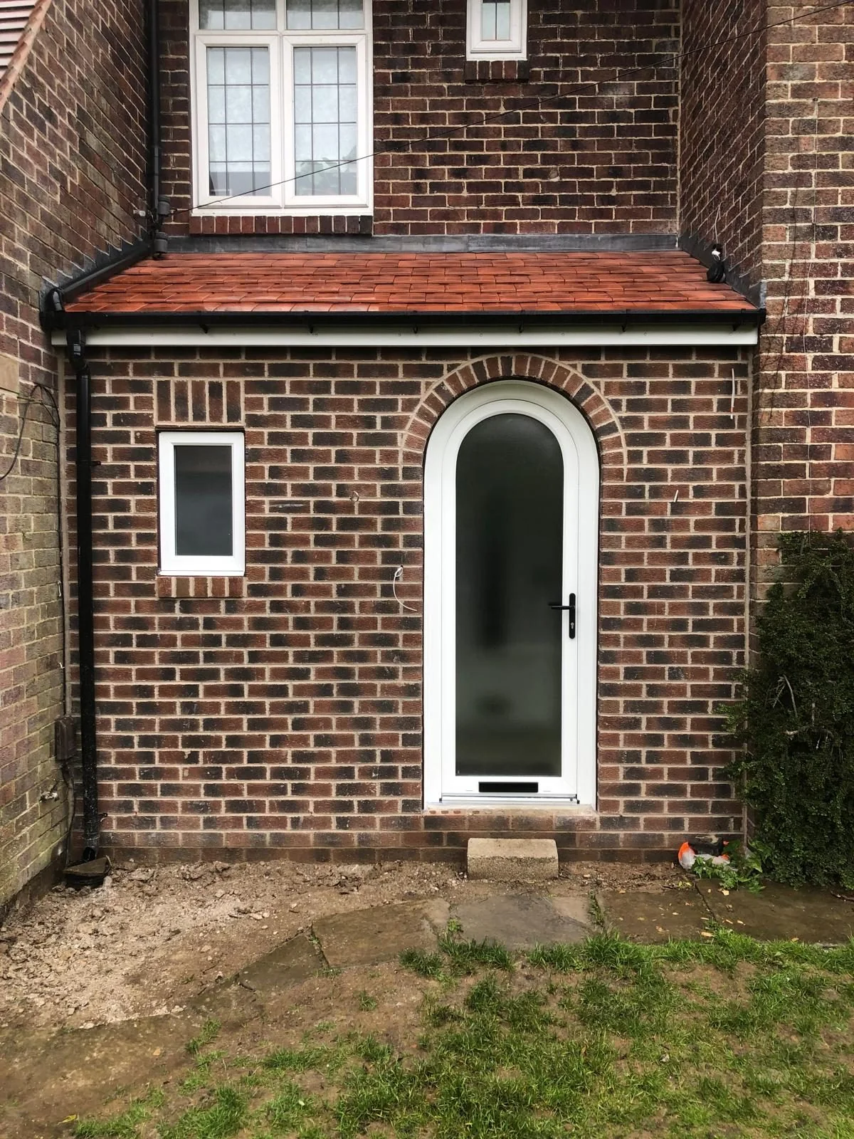 Brick entrance porch with arched front door and small side window