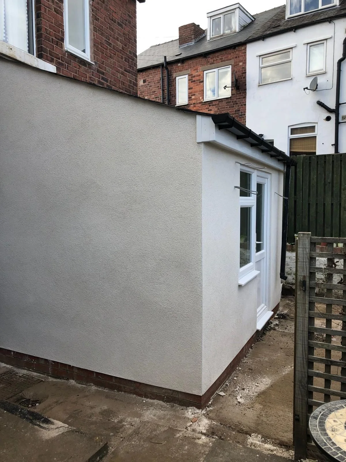 White rendered side extension with a small window and sloping roof
