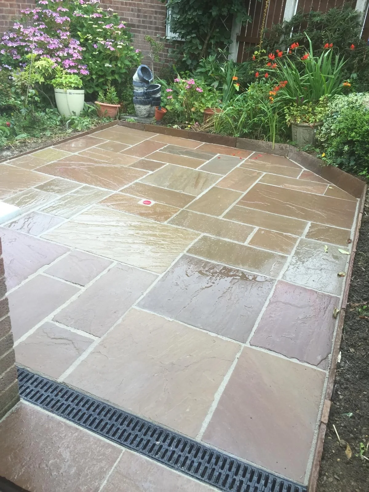 Stone slab patio with inset drainage channel beside planted borders