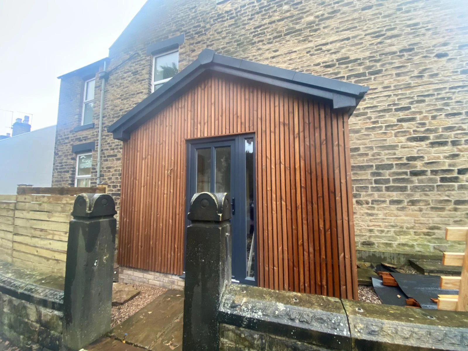 Finished timber clad entrance porch beside a stone house